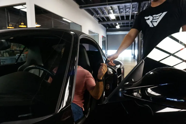 Professional automotive detailing studio discussing service pricing with a customer while detailing a luxury vehicle